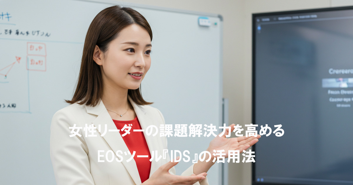 白いスーツと赤いインナーを着た日本人女性リーダーが、会議室でホワイトボードとモニターを使いながら課題解決について説明している様子