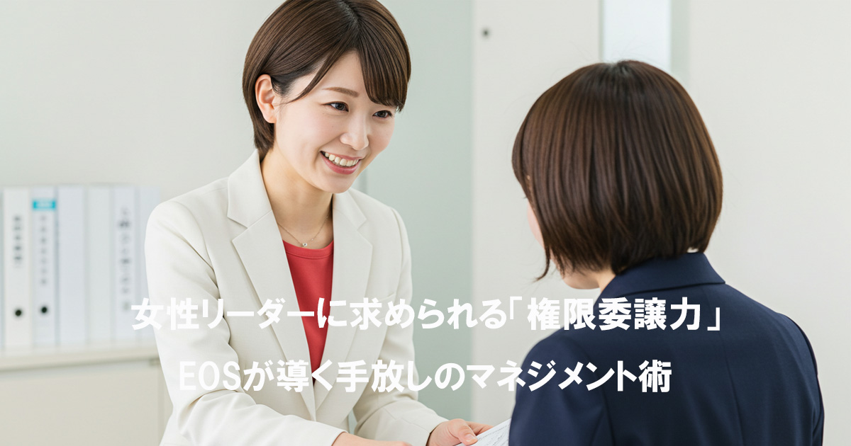 白いスーツと赤いインナーを着た女性リーダーが、部下と笑顔でコミュニケーションをとっている様子。権限委譲について話しているビジネスシーン。